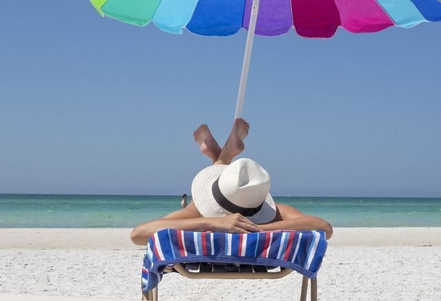 Žena na lehátku na pláži pod slnečníkom
